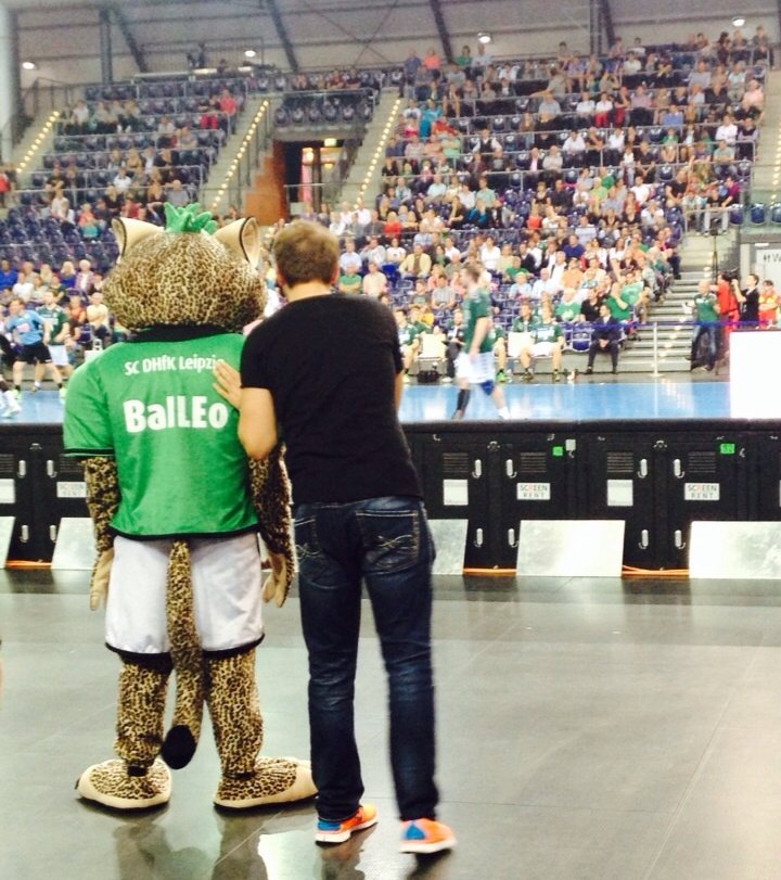 Coach mit dem Arm um ein Maskottchen in der Halle