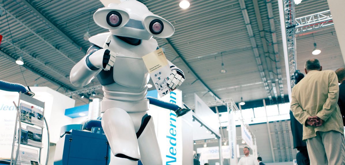 Maskottchen-Roboter am Messestand verteilt Flyer
