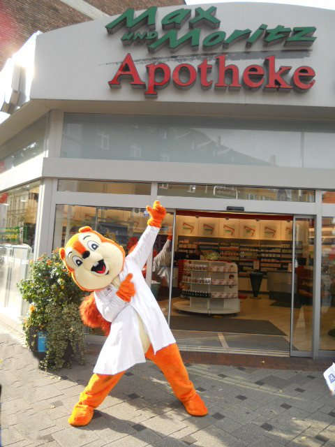 Maskottchen als Apotheker vor einer Apotheke